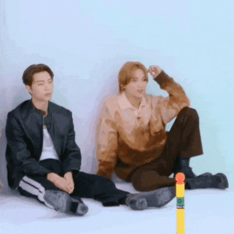 two men are sitting on the floor next to each other and a yellow pole .