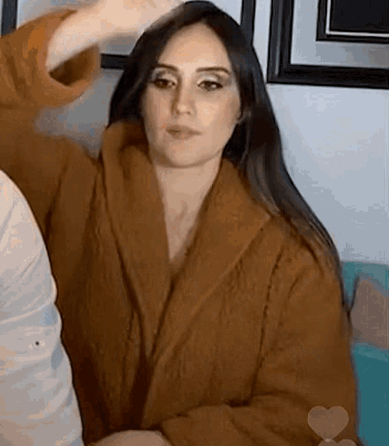 a woman in a brown robe is sitting on a couch and looking at the camera .