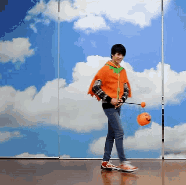 a man in an orange cape is holding an orange ball in front of a blue sky