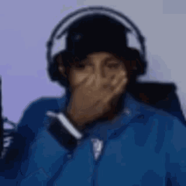 a man wearing headphones and a blue jacket is covering his face with his hands .