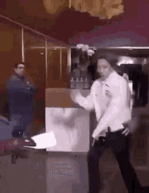a man in a white shirt is dancing in a restaurant while a man stands behind him .