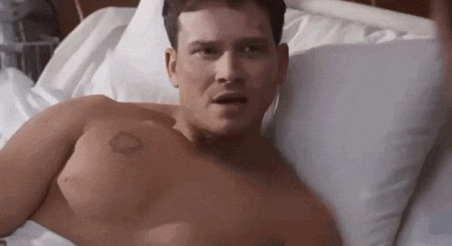 a shirtless man is laying in a hospital bed with a tattoo on his chest