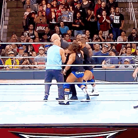 a wrestler in a blue tank top is fighting another wrestler in a black tank top in a wrestling ring