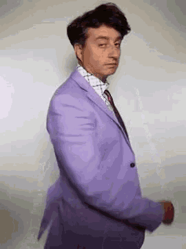 a man is wearing a purple suit and tie and dancing .