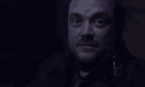 a man with a beard is making a funny face in a dark room while pointing at his head .