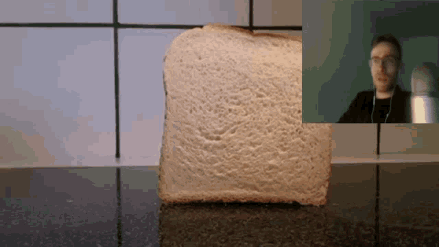 a slice of bread is sitting on a counter next to a man wearing glasses