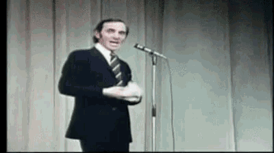 a man in a suit and tie is singing into a microphone on stage .