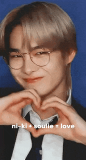 a man wearing glasses and a suit is making a heart with his hands .
