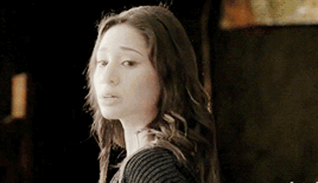 a woman with long dark hair is wearing a black sweater and looking at the camera .