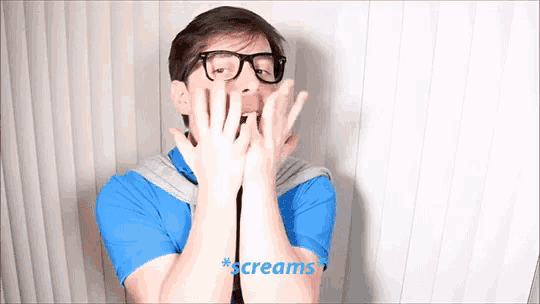 a man with glasses is screaming with his hands in front of his face
