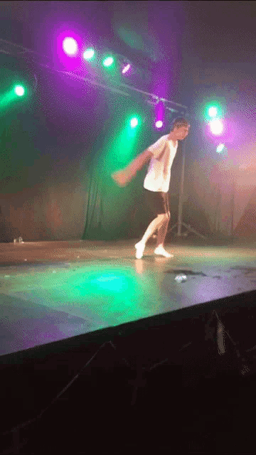 a man is dancing on a stage under purple and green lights