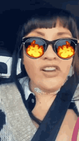 a woman in a car wearing sunglasses with flames reflected in them
