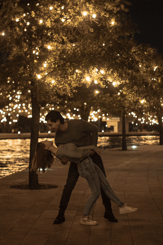 a man is holding a woman in his arms in front of a tree with lights