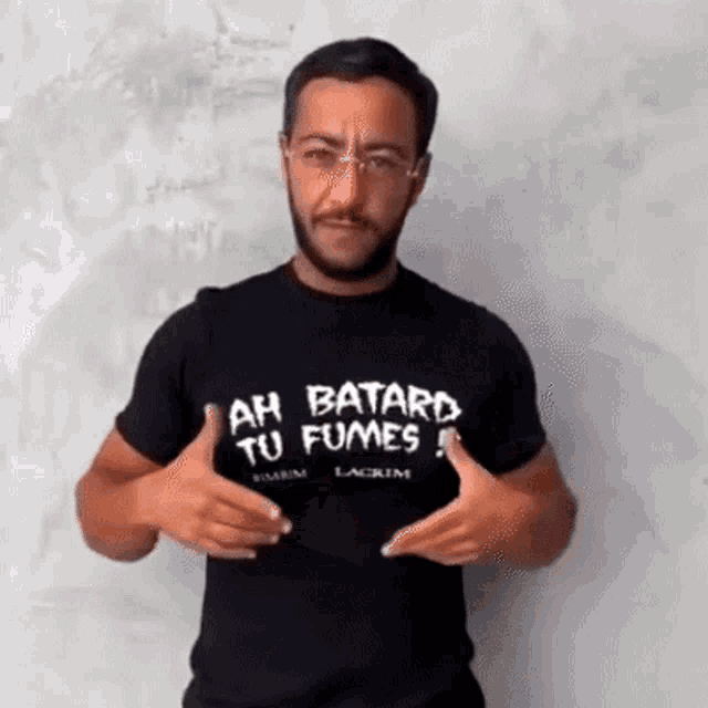 a man wearing a black shirt with ah batard tu fumes on it