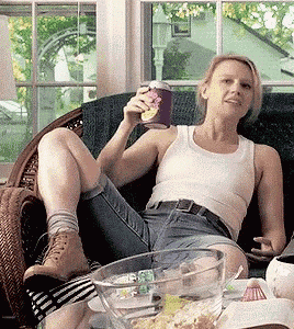 a woman in a white tank top is sitting on a couch holding a can of ice cream
