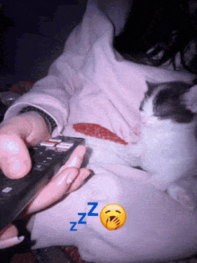 a person holding a remote control while a cat sleeps