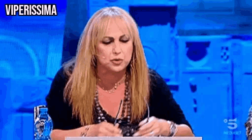 a woman with long blonde hair is sitting at a table with a pen in her hand and a sign that says viperissima .