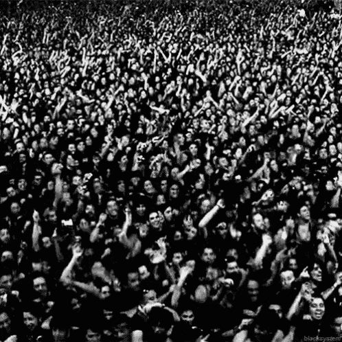 a black and white photo of a crowd of people raising their hands in the air at a concert .
