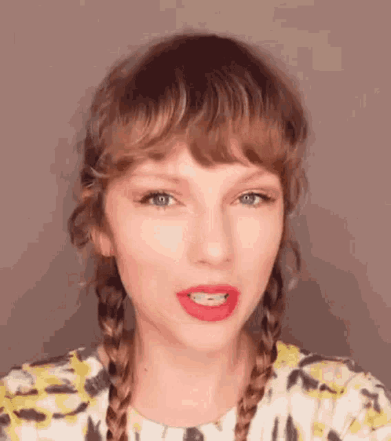 taylor swift is wearing braids and red lipstick while making a funny face .