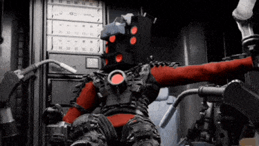 a robot with a red head is sitting in a chair in front of a computer