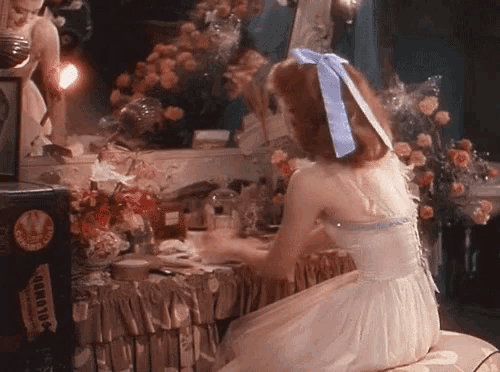 a woman in a white dress with a blue bow in her hair sits in front of a clock that says ' clock '