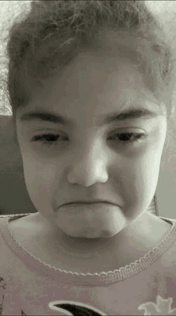 a little girl in a pink shirt is making a funny face