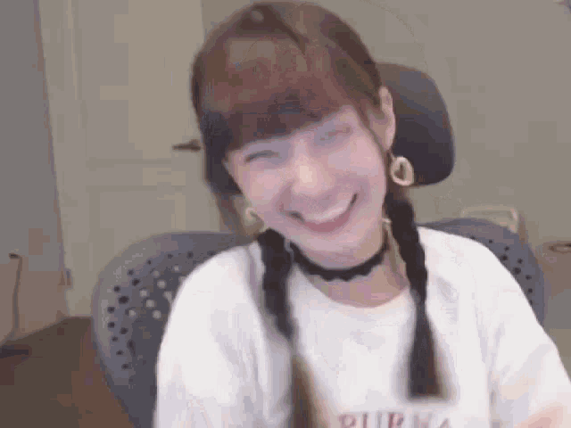 a woman with braids is smiling while sitting in a chair in a room .
