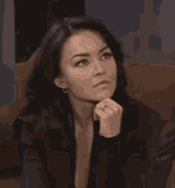 a woman is sitting on a couch with her hand on her chin and looking to the side .