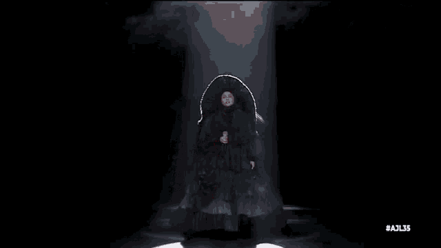 a man in a cape is dancing in a dark room in front of a crowd .