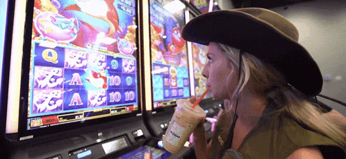 a woman in a cowboy hat drinks from a straw in front of a slot machine