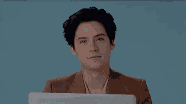 a young man in a brown jacket is holding a laptop computer and smiling .