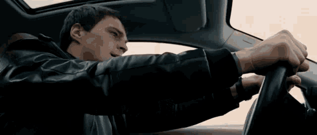 a man in a leather jacket is driving a car with the sunroof open
