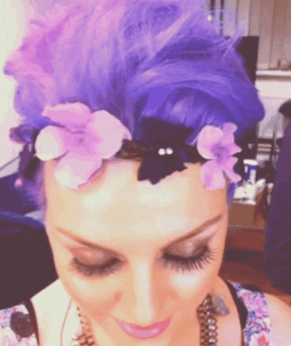 a woman with purple hair has a black cat on her head