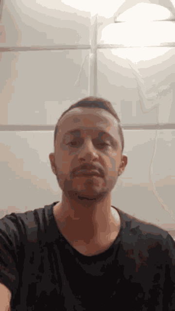 a man with a beard wearing a black shirt looks at the camera with his eyes closed