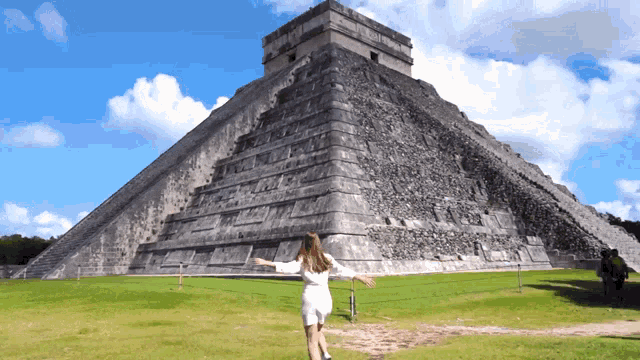 a woman is standing in front of a large stone pyramid