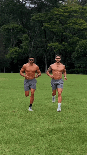 two shirtless men are running in a grassy field and one has the word jesus on his chest