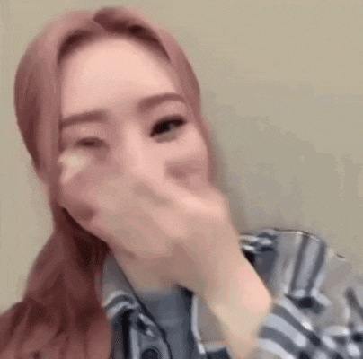 a woman is covering her mouth with her hand while wearing a plaid shirt .