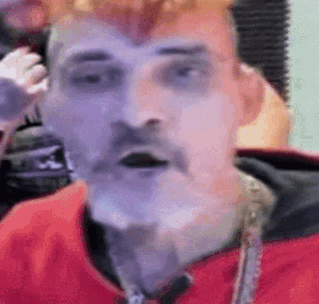 a man with red hair and a mustache is wearing a red jacket and a gold chain around his neck .