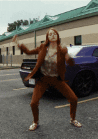 a woman is dancing on the street in front of a blue car