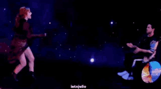 a man in a wheelchair is dancing with a woman in a dress in front of a planet .