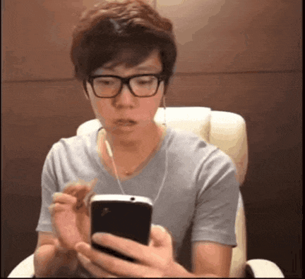 a man wearing glasses is sitting in a chair looking at a cell phone .