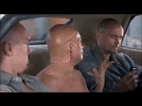 three bald men are sitting in the back seat of a car looking at a cell phone .