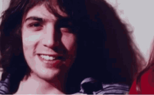 a close up of a man 's face with long hair smiling and looking at the camera .