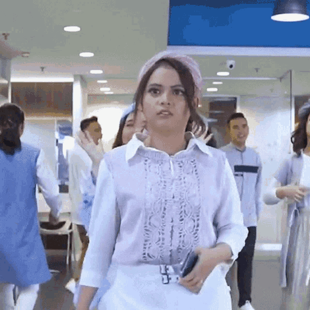 a woman wearing a white shirt and a pink headband is walking in a hallway
