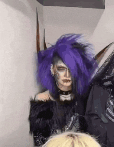 a woman with purple hair and horns is standing next to a man with blonde hair .