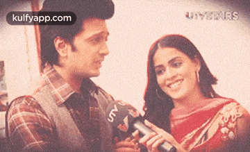 a man is holding a microphone in front of a woman who is smiling .
