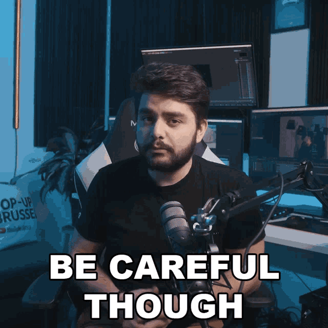 a man sitting in front of a microphone with the words be careful though below him