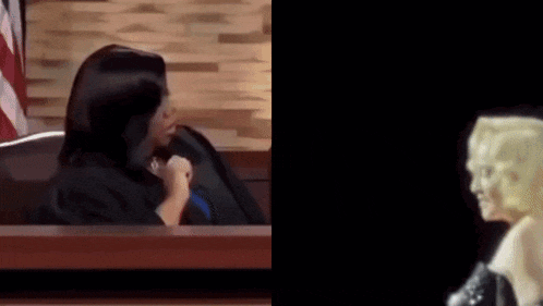a woman in a judge 's robe is sitting in a courtroom next to a woman in a wig .