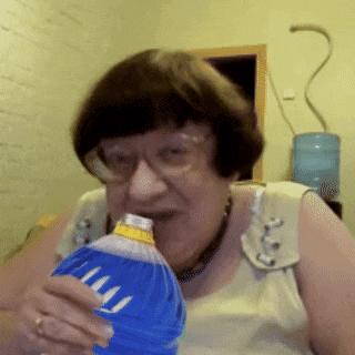 a woman with glasses is drinking from a blue bottle with the letter m on the label