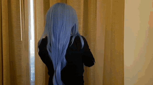 a person with long blue hair stands in front of a window